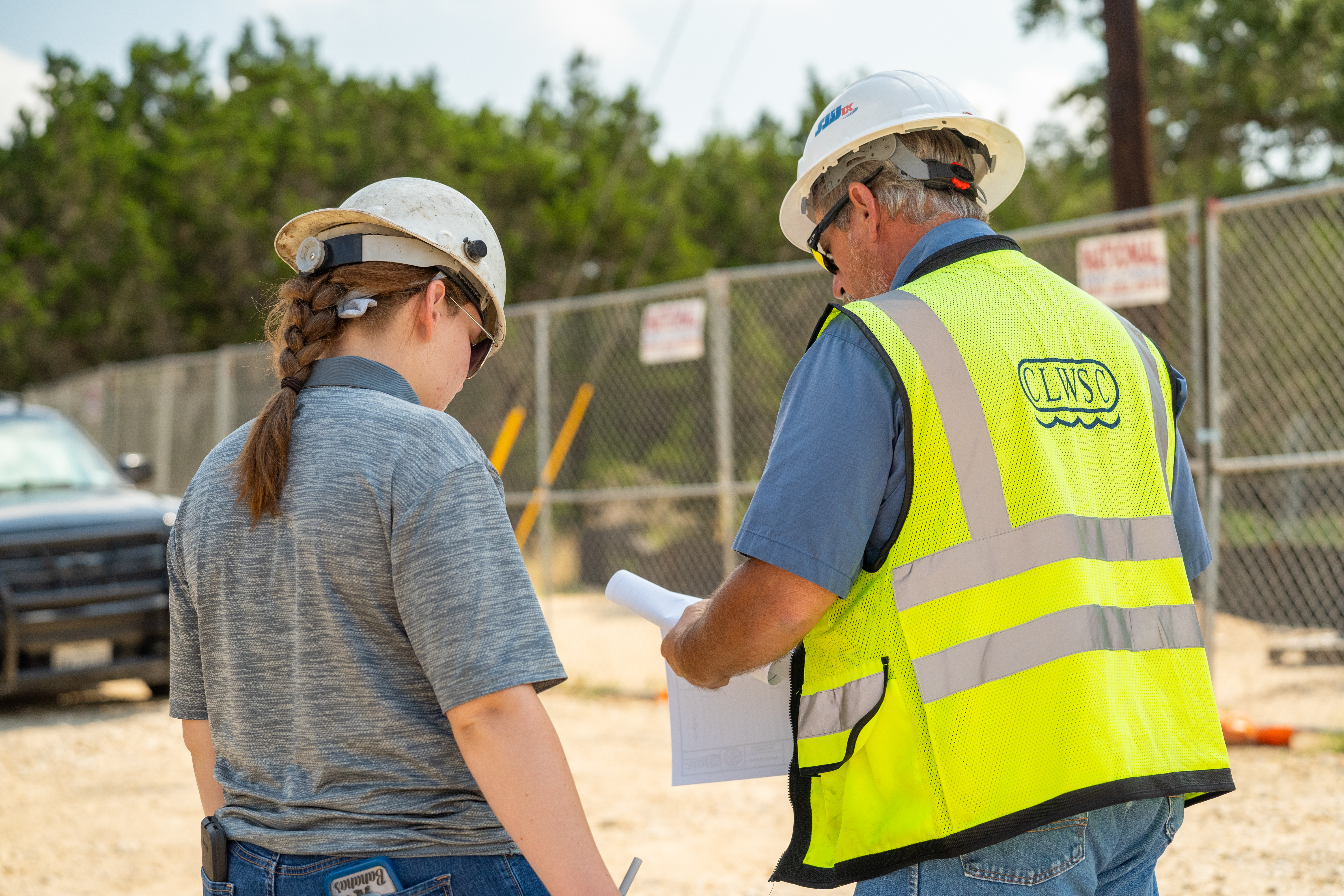 two employees wearing hard hats looking at paper